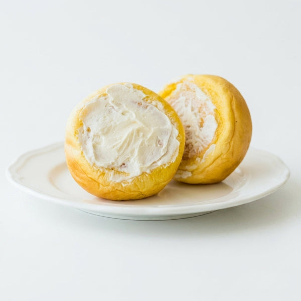 Two halves of a yellow fruit filled with white cream on a white plate.