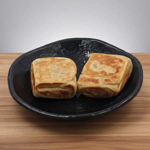 Two pieces of Vegetable Rotti flatbread on a black plate with red chili peppers beside them, on a yellow background.